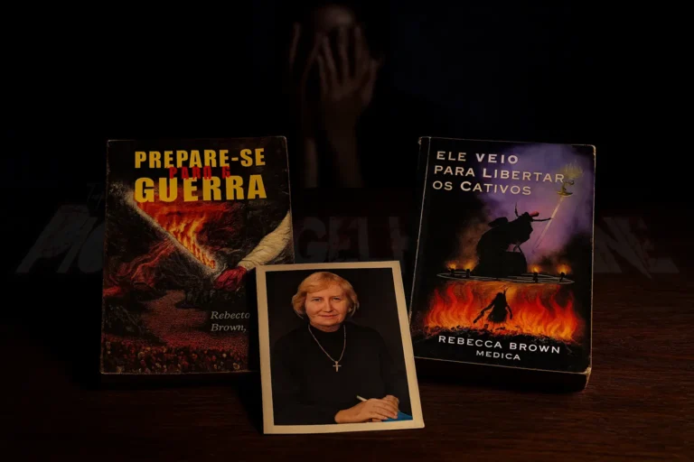 Cenário de investigação criminal sobre mesa de madeira escura: exemplares físicos e desgastados dos livros 'Prepare-se para a Guerra' e 'Ele Veio Libertar os Cativos'. Ao centro, uma fotografia impressa de Rebecca Brown (Ruth Bailey) vestindo preto e cordão com cruz. Ao fundo, na penumbra, silhueta de uma pessoa com mãos no rosto em desespero.